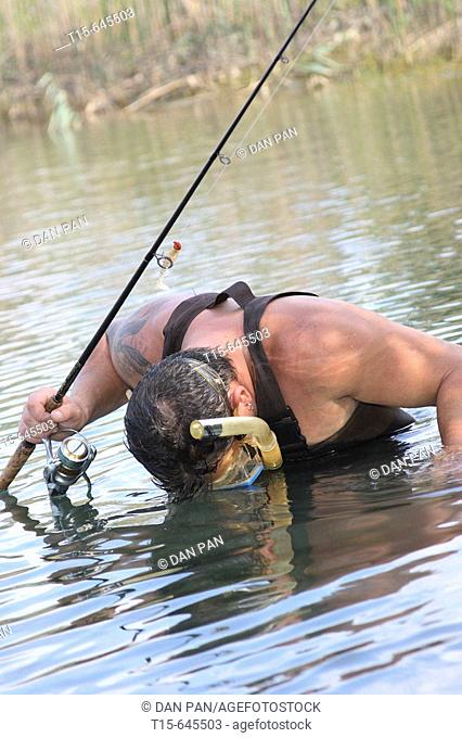 Man in his 30's holding a fishing rod wearing snorkel mask looking for fish in the lake