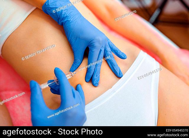 Cosmetician in gloves gives botox injection in the stomach to female patient on treatment table. Rejuvenation procedure in beautician salon