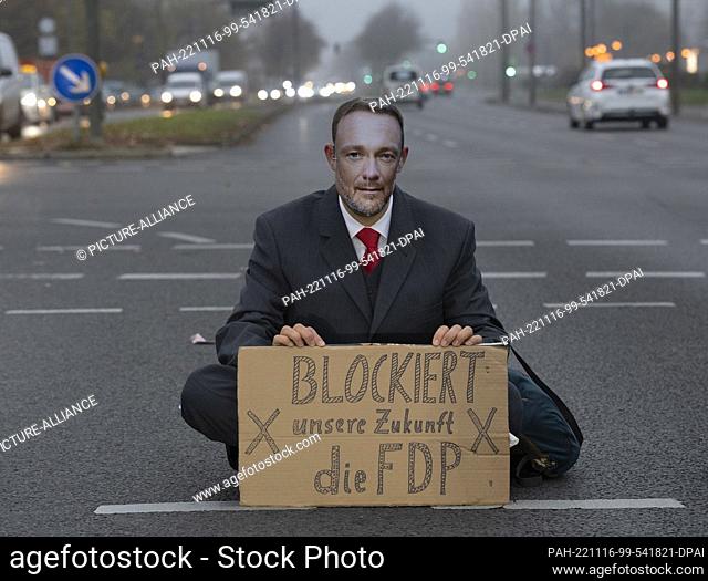 16 November 2022, Berlin: An activist of the group ""Last Generation"" sits on an intersection at Landsberger Allee and wears a face mask showing Federal...