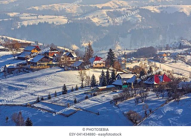 Countryside landscape with traditional Romanian village in the valleys of Bucegi mountains on a sunny cold winter morning in Pestera, Brasov county