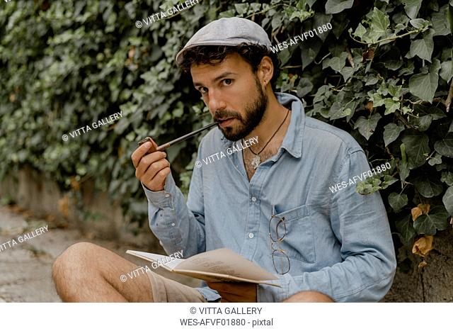 Young man smoking pipe, reading a book