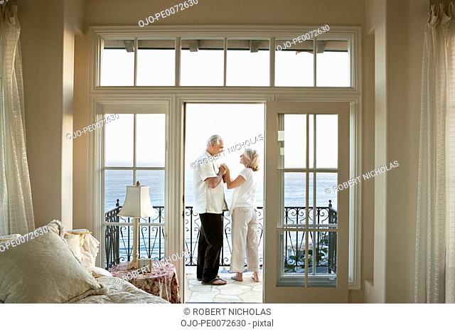 Senior couple holding hands face to face on balcony overlooking ocean