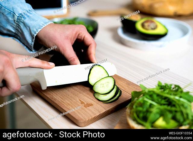 Hands of woman slicing cucumber on cutting board