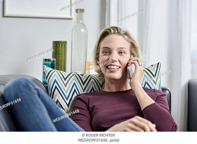 Smiling young woman on cell phone lying on couch at home