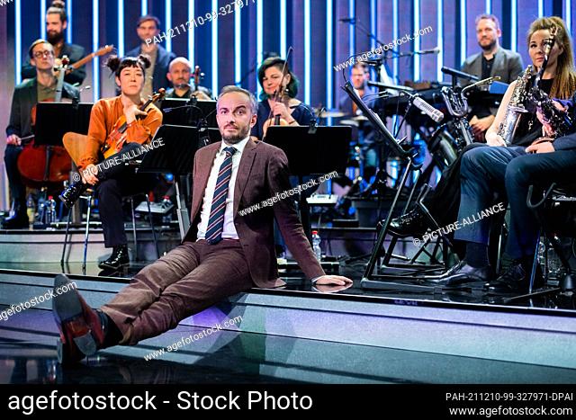02 December 2021, North Rhine-Westphalia, Cologne: Jan Böhmermann, presenter, sits in front of his orchestra, the Rundfunk Tanzorchester Ehrenfeld
