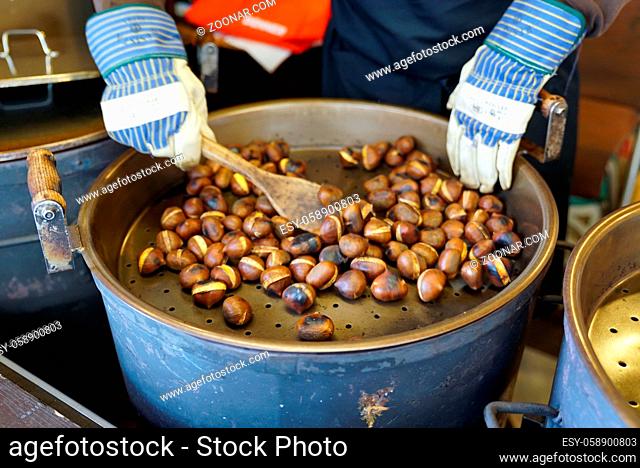 View of male hands stirring and roasting delicious organic chestnuts on a gas barrel stove with wooden ladle