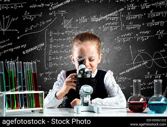 Little girl scientist looking through microscope in classroom at chemistry lesson. School chemical laboratory with glass flasks and test tubes