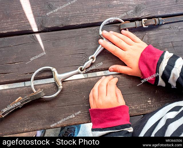 Girl preparing steel horse snaffle-bit on wooden table at stable