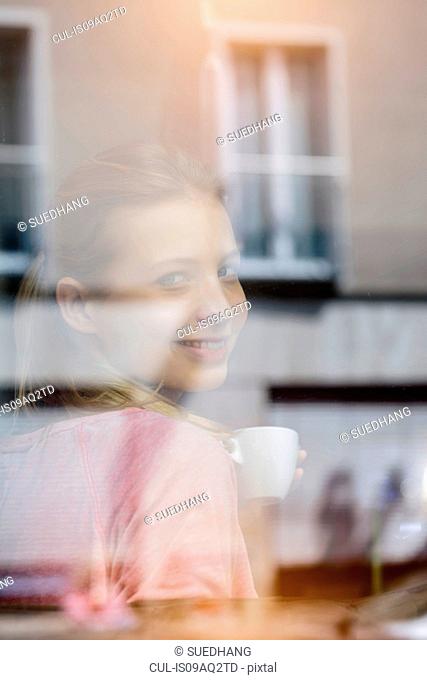 Portrait of young woman drinking coffee looking through cafe window