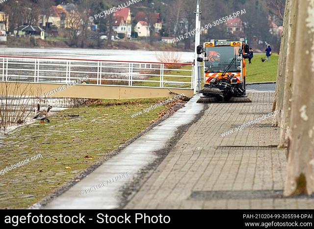 03 February 2021, Saxony, Pirna: A man drives a sweeper on the riverbank. In the coming days, this spot could already be flooded by water