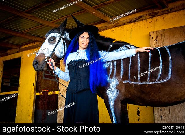 Halloween celebration, a young girl in a witch costume stands by a horse with a skeleton drawn