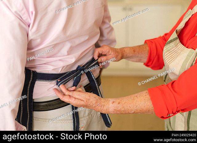 Mid section of senior caucasian couple tying apron in kitchen. retreat, retirement and happy senior lifestyle concept. || Model approval available