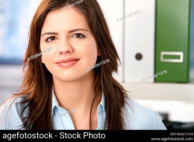 Pretty professional girl smiling at camera, face in closeup, office background