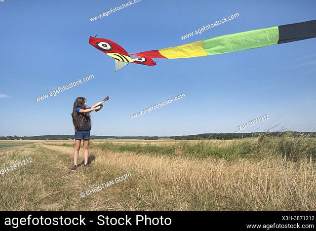 Young girl in denim shorts and blue shirt flying a Chinese kite in a flat landscape in Centre-Val de Loire region, France