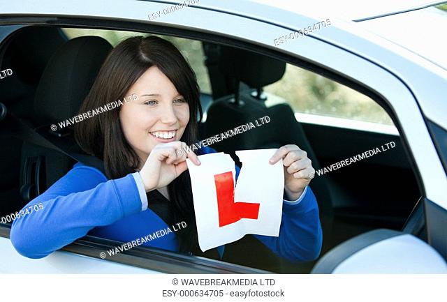 Joyful teen girl sitting in her car tearing a L-sign after having her drivers licence