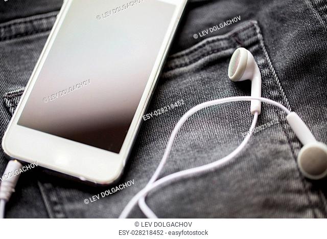 technology and music concept - smartphone and earphones on pocket of denim pants or jeans
