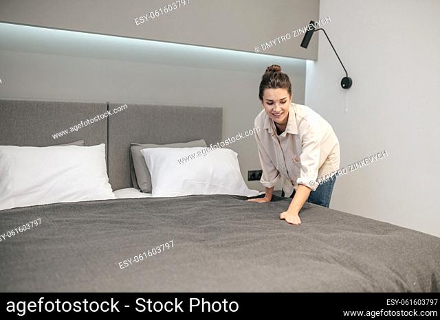 Making bed. A young woman making bed and looking positive
