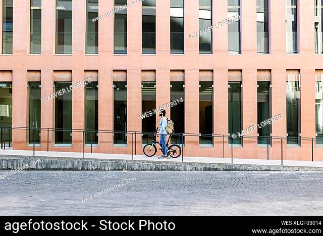 Man wheeling with bicycle by building