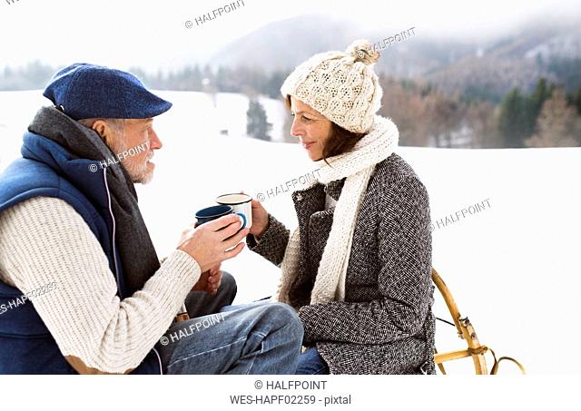 Senior couple having a break with hot beverages in snow-covered winter landscape