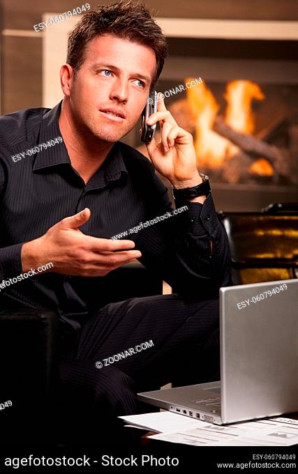 Businessman sitting at home, in front of fireplace, talking on phone, gesturing