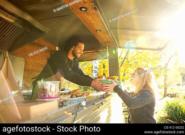 Happy food truck owner serving food to customer in sunny park