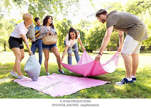 friends arranging place for picnic at summer park