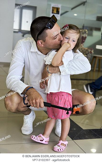 father kissing toddler daughter indoors, holding action camera in hand