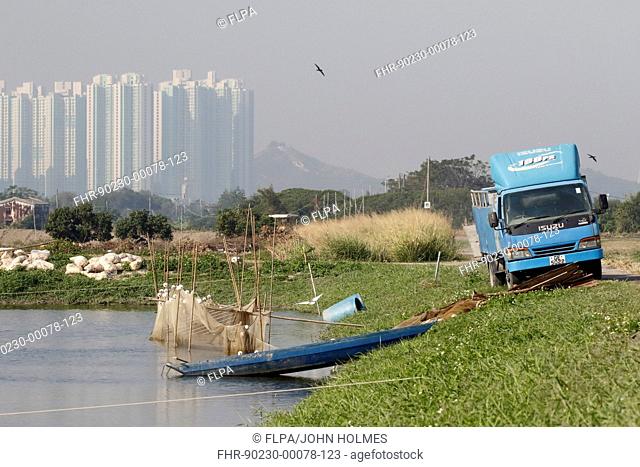 Commercial fishpond with sacks of fish food (bread crusts), boat, net and lorry, with skyscrapers in background, Tai Sang Wai, New Territories, Hong Kong, China
