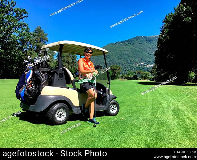 Woman Leaning on a Golf Cart on the Fairway with Mountain in Background in a Sunny Day in Switzerland