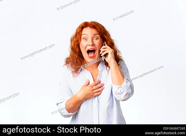 Surprised and excited, happy smiling redhead woman found out amazing news via cellphone, talking on mobile phone, being informed about winning