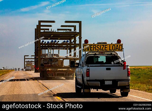 Oversize loaded truck traveling along road at a sunny day. Pickup following behind for security. Coutryside grasslands and plains in the background