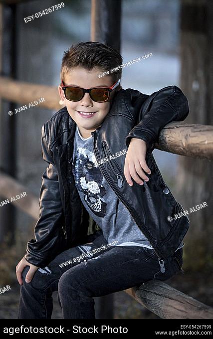 Stylish little boy in sunglasses and brutal outfit posing with confidence at camera