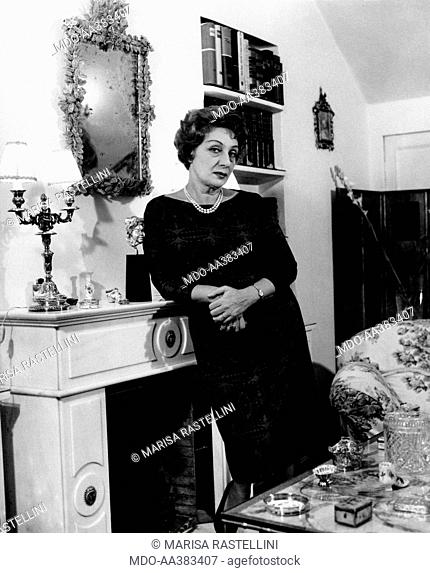 Portrait of Andreina Pagnani at home. Italian actress Andreina Pagnani (Andreina Gentili) leaning on the fireplace in her house. Rome, 1964