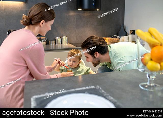 Feeding a baby. Parents feeding a cute baby boy in the kitchen