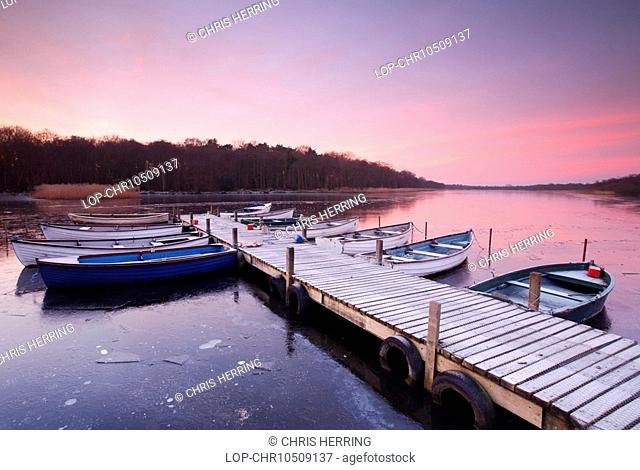 England, Norfolk, Ormesby Broads, Sunrise over rowing boats tied to a jetty on the frozen water of Ormesby Broads in the Broads National Park in Norfolk