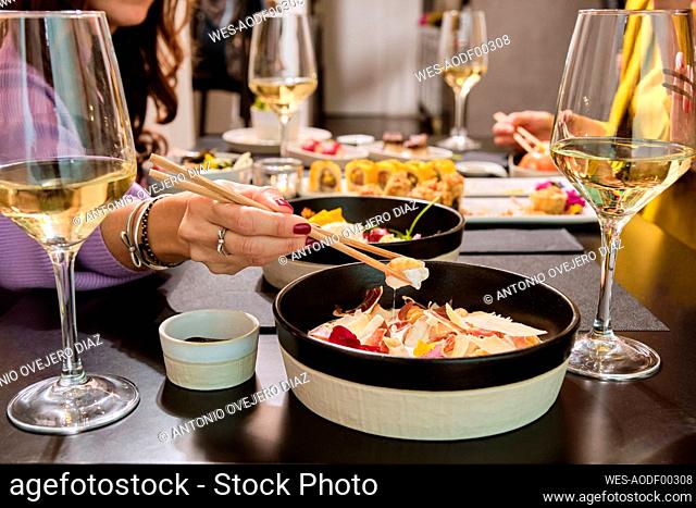 Woman having food with chopsticks while sitting with friends at restaurant