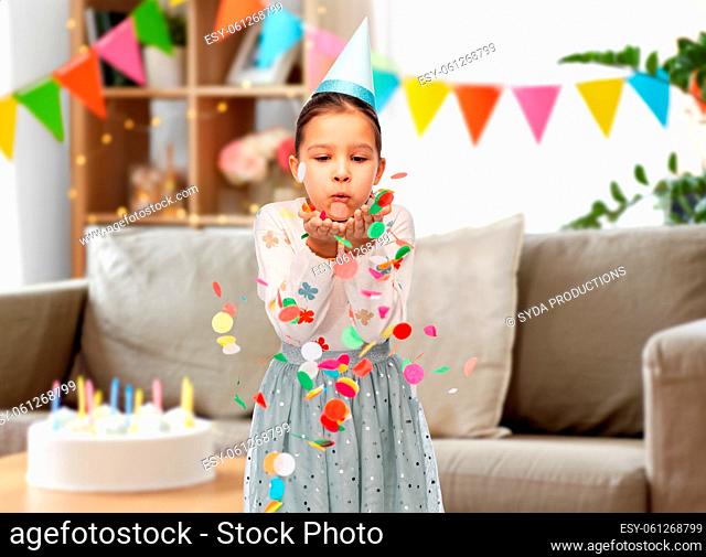 girl in birthday party hat blowing to confetti