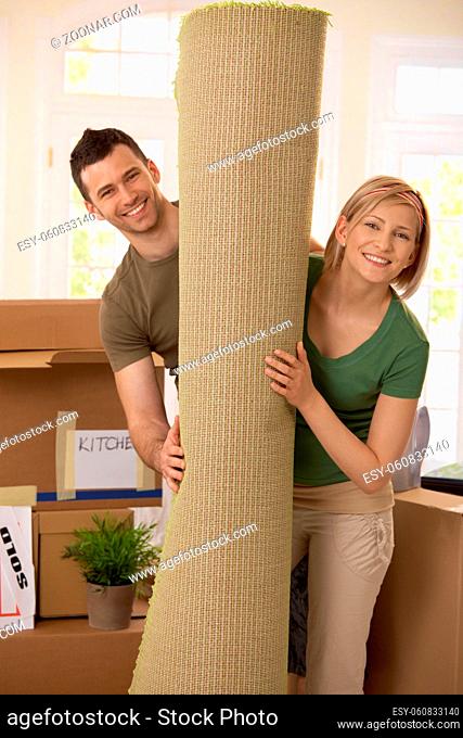 Portrait of smiling couple moving house, holding carpet rolled up, surrounded with boxes