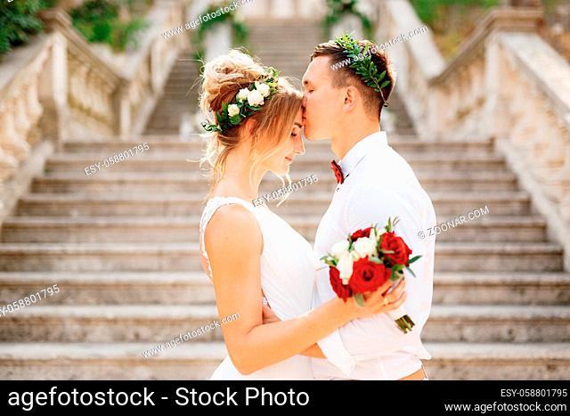 The bride and groom in wreaths stand hugging and kissing on the stairs of the ancient church in Prcanj, close-up. High quality photo