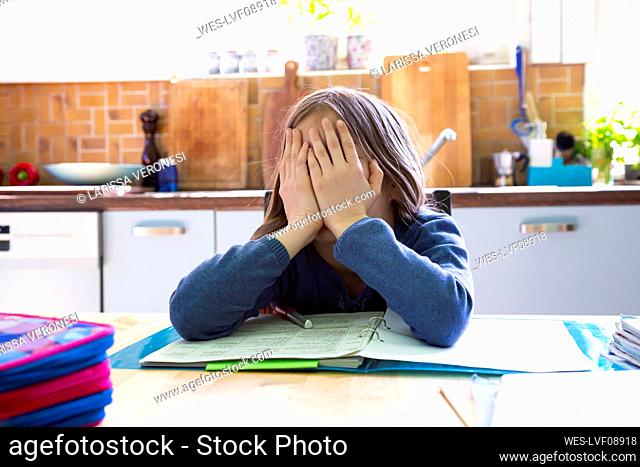 Girl doing homework in kitchen at home, hands on face