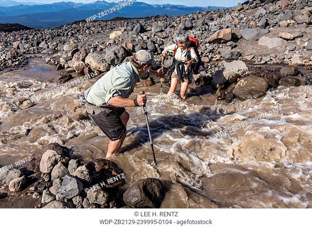 Lee Rentz assisting Junko Waibel in crossing the raging brown waters of a branch of Muddy Fork Creek coming off Lyman Glacier on Mt. Adams, Mt