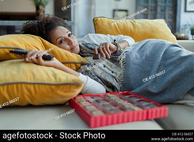 Cozy woman eating chocolates and watching TV on living room sofa
