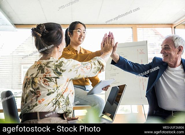 Successful business colleagues giving high-five to each other in office