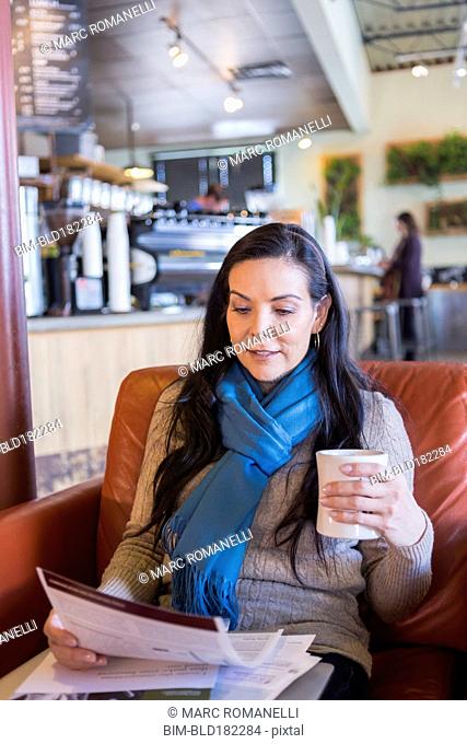 Hispanic woman reading paperwork in cafe