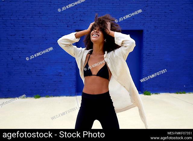 Young woman with hand in hair screaming in front of blue wall