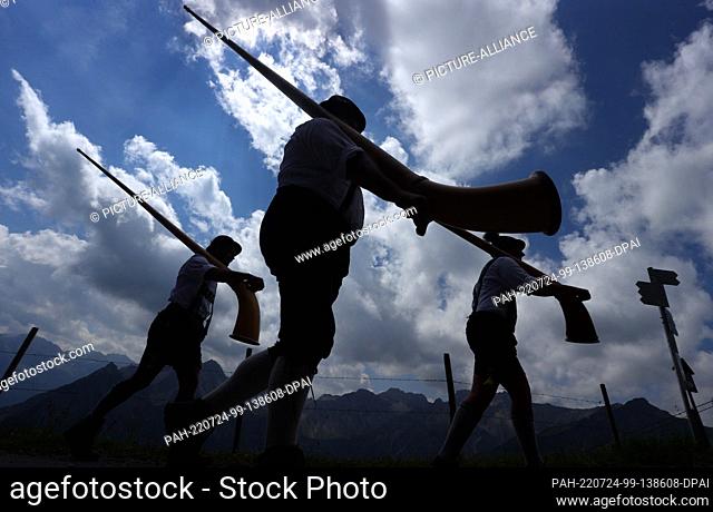 24 July 2022, Bavaria, Oberstdorf: Members of the alphorn group EUREGIO via salina walk with their alphorns against a partly cloudy sky after the 30th...