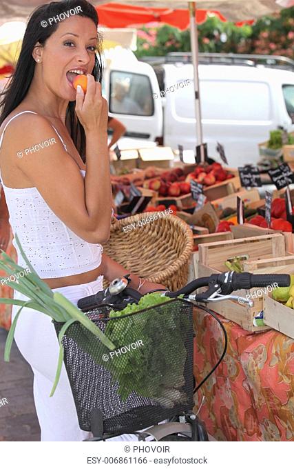 Summery woman eating an apricot at a market stall