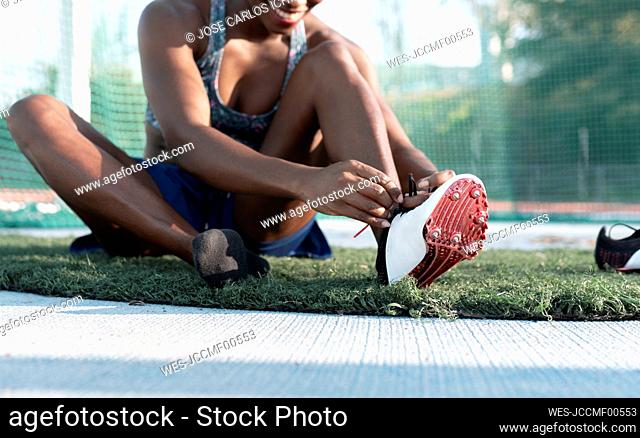 Female athlete tying shoelace while siting in sports court against net