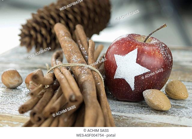 Christmas apple with snow star, cinnamon sticks, fir cones, almonds and hazelnuts on table