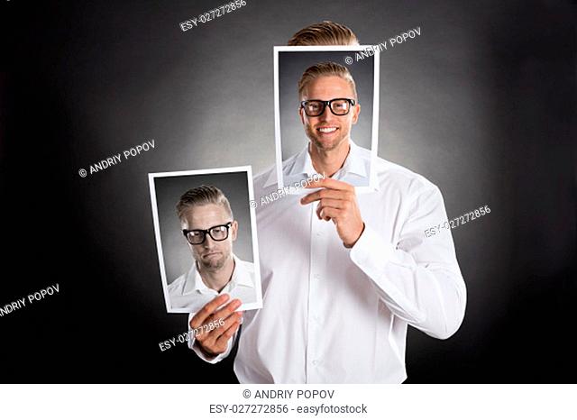 Sad Man Holding Smiling Picture In Front Of His Face Against Black Background